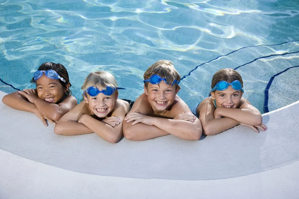 Four smiling children resting on the edge of a pool