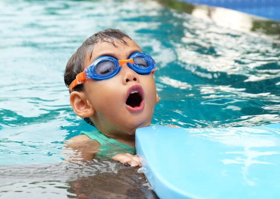 Young child with goggles floating with a kickboard